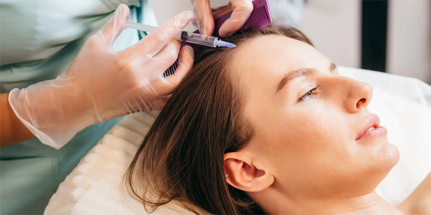 Stammzellen-Behandlung bei Hairmedic: Eine junge Frau liegt entspannt auf einer Behandlungsliege, während eine Fachperson mit transparenten Handschuhen eine gezielte Injektion in den vorderen Haaransatz durchführt. Die Szene stellt eine moderne Form der Haarbehandlung dar – die Stammzellen-Therapie –, bei der regenerative Wirkstoffe direkt in die Kopfhaut eingebracht werden, um das Haarwachstum anzuregen und Haarausfall bei Frauen zu behandeln.